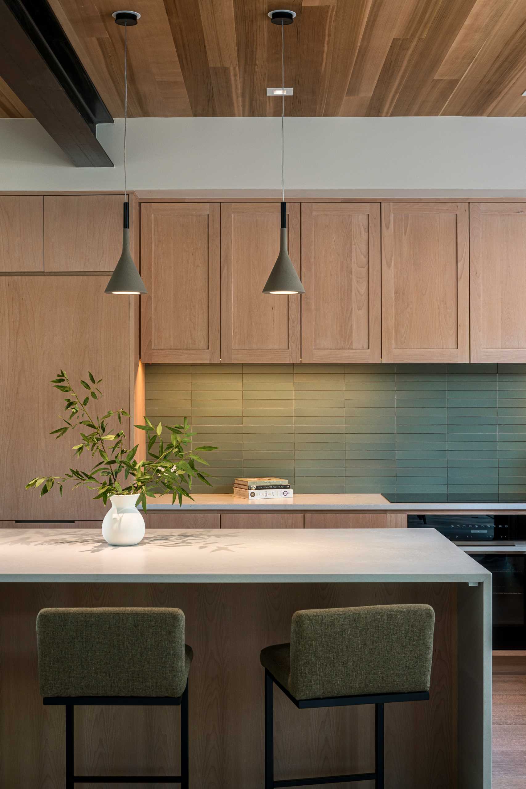 This modern kitchen has a wood ceiling, light wood cabinets, and a green tile backsplash.