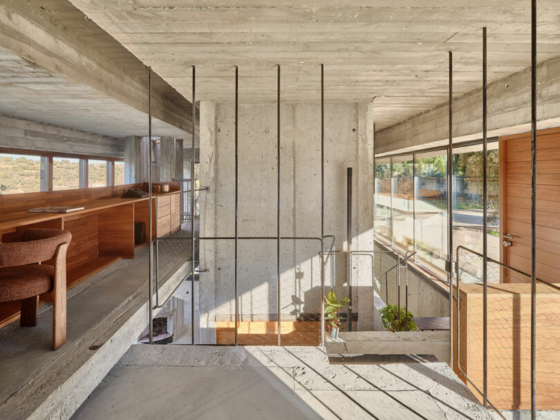 Interior of a modern home featuring concrete walls, a wooden dining area, metal railings, large windows, and a staircase with plants.