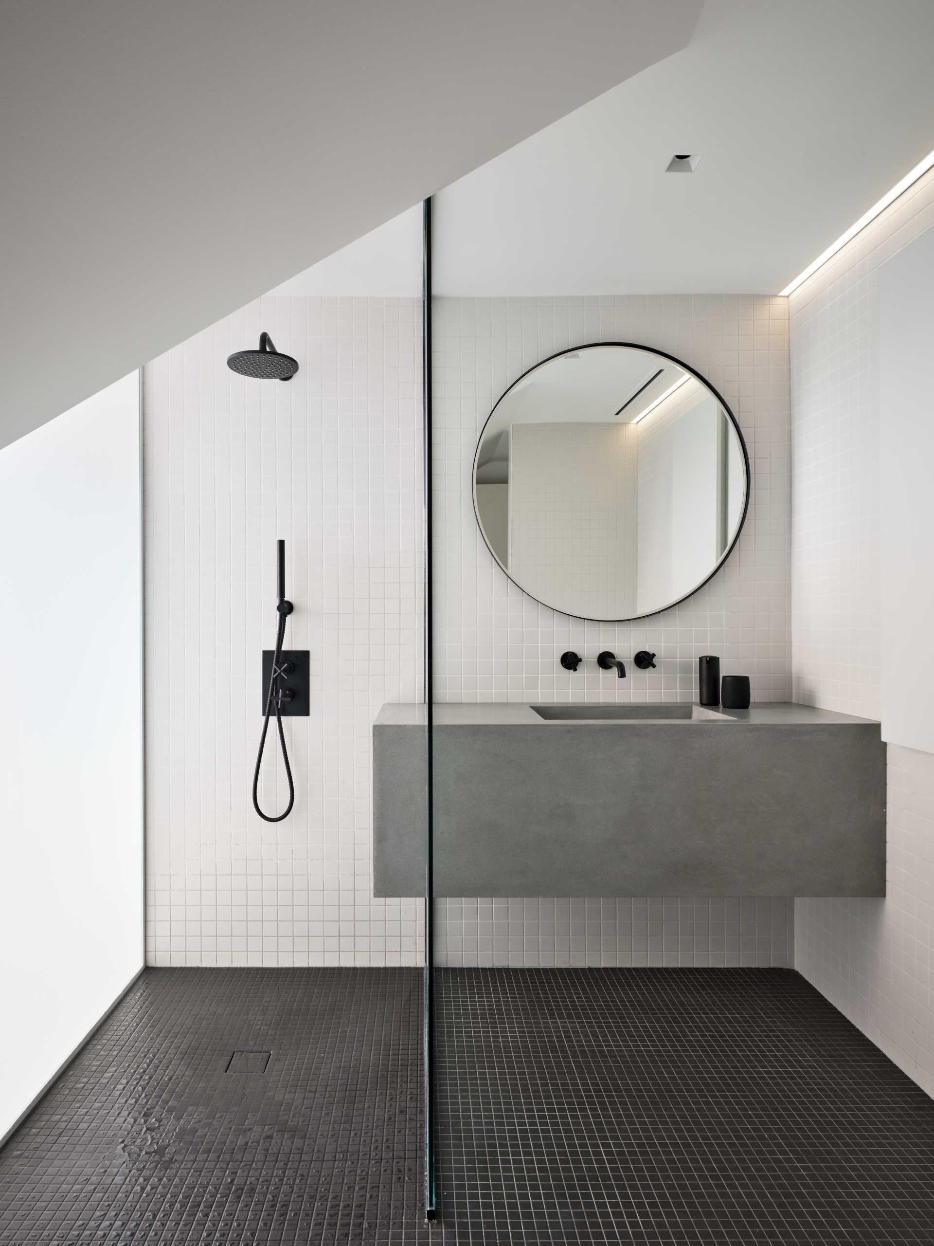 This bathroom is minimalist in its design, with square white tiles covering the walls, and black tiles on the floor.