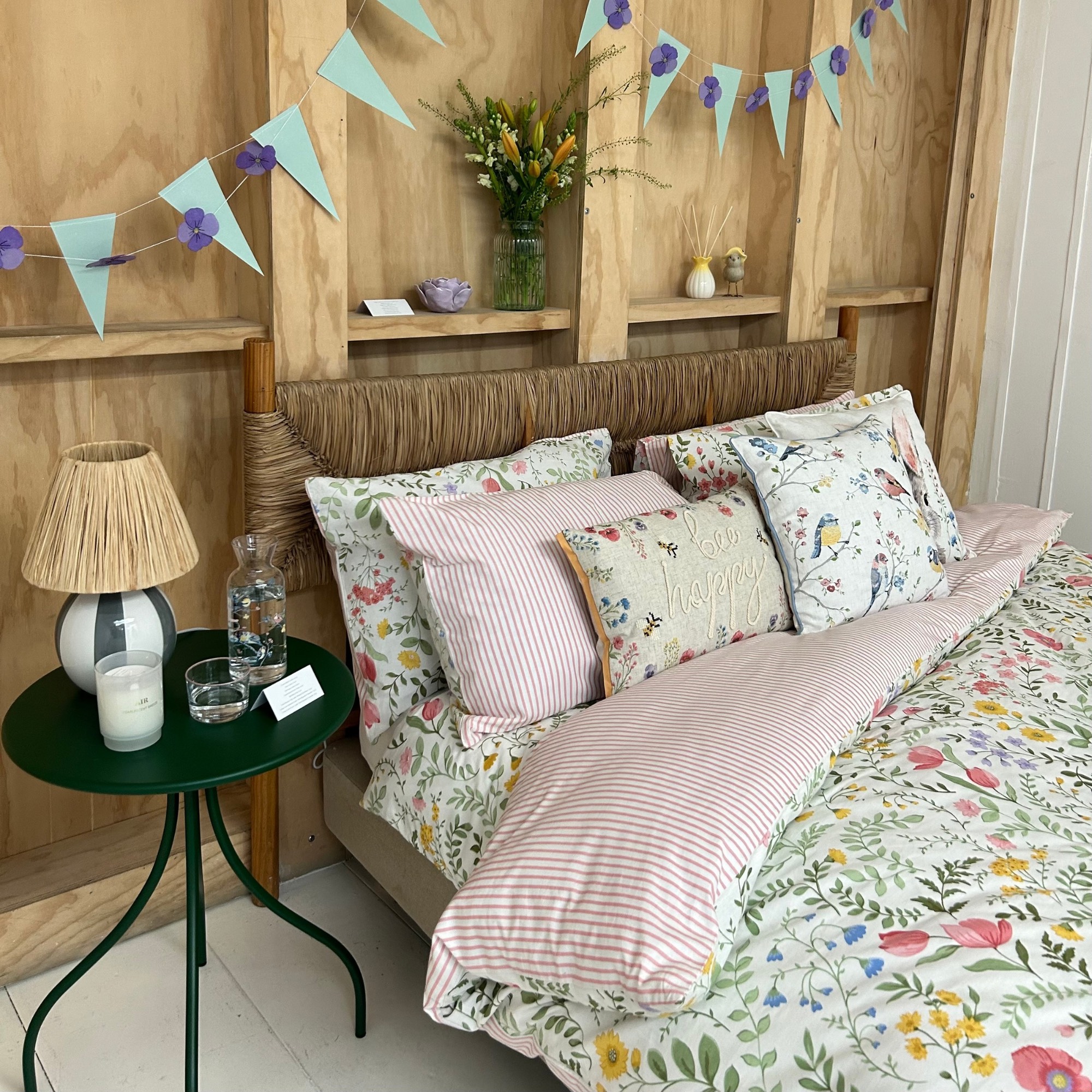 A pale floral and striped bedding set with a dark green bedside table next to it