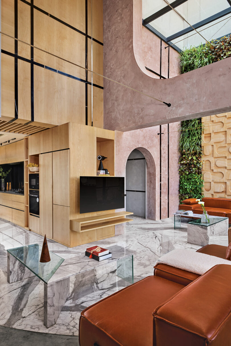 Modern living room with high ceilings, marble floors, leather seating, glass tables, a TV, and a vertical garden wall. Features wooden and textured walls, and an arched doorway.