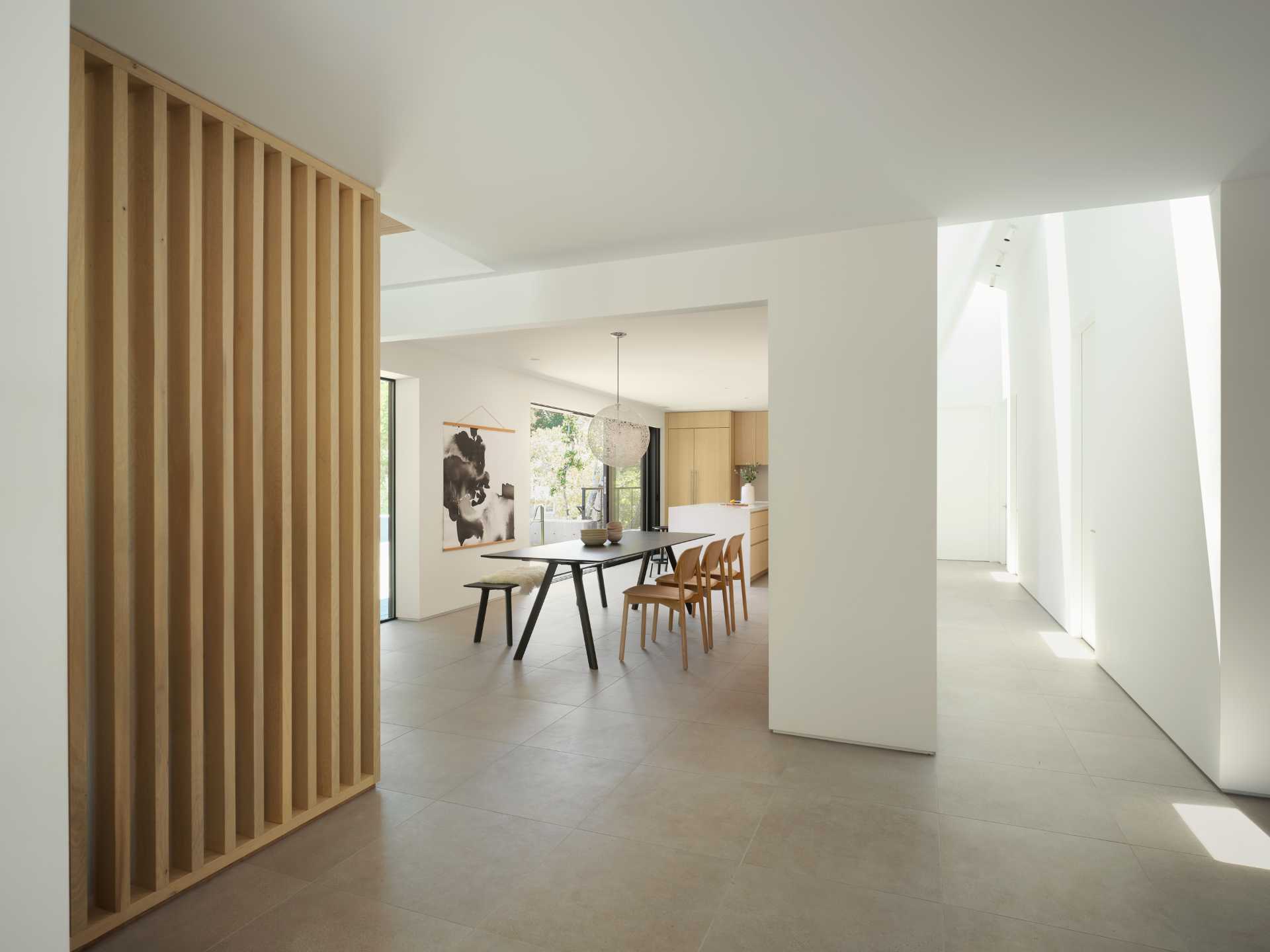 An open-plan dining room and modern kitchen with wood cabinets and an island, opens up to the deck through a sliding door.