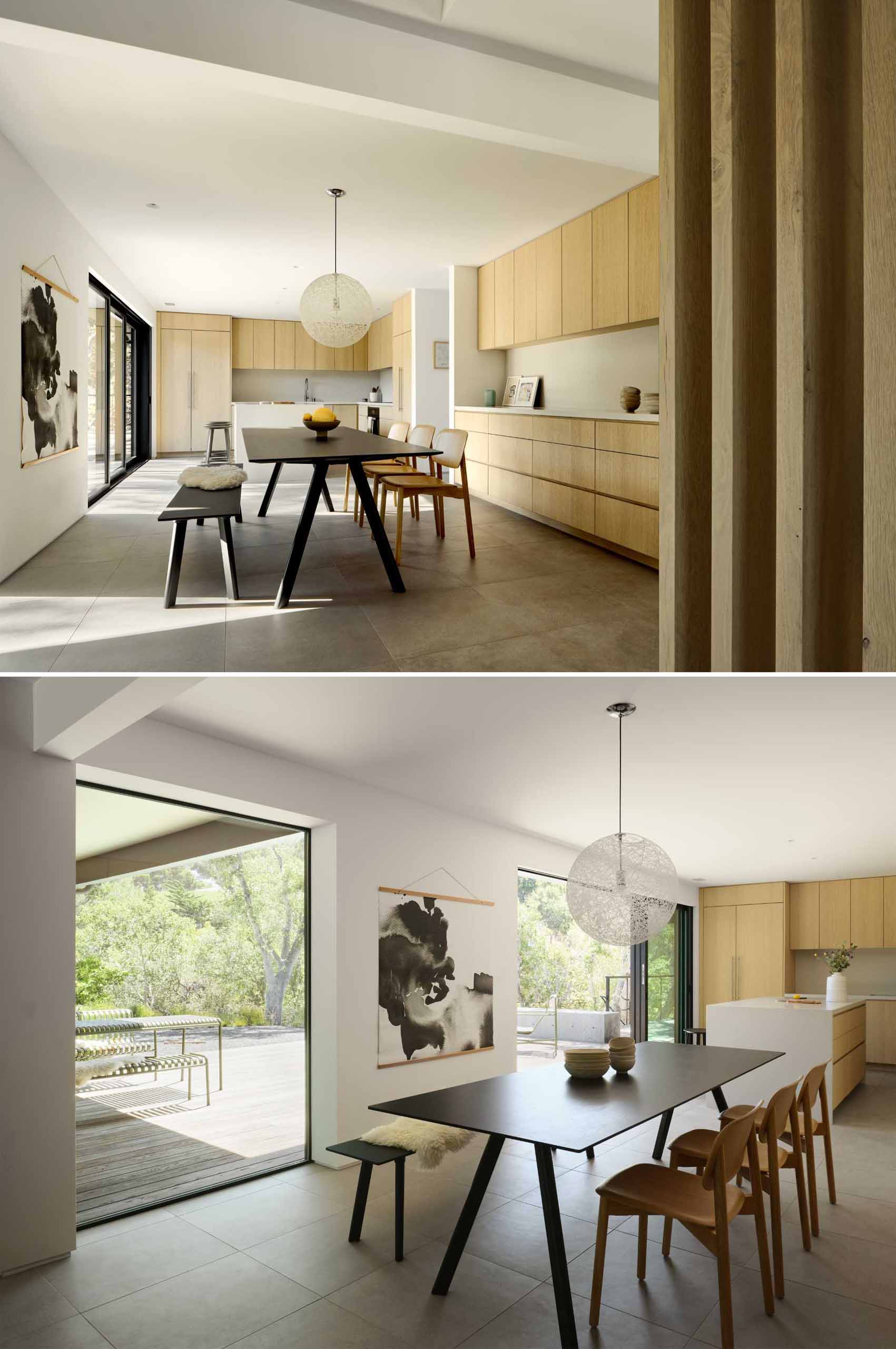An open-plan dining room and modern kitchen with wood cabinets and an island, opens up to the deck through a sliding door.