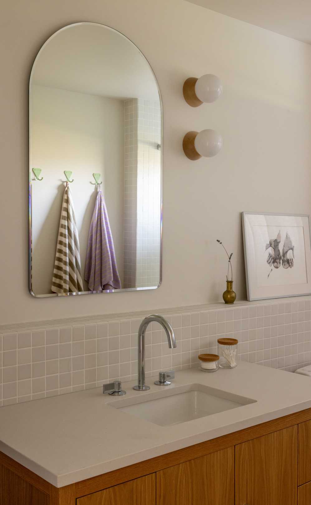 A contemporary bathroom with square tiles and an arched mirror.
