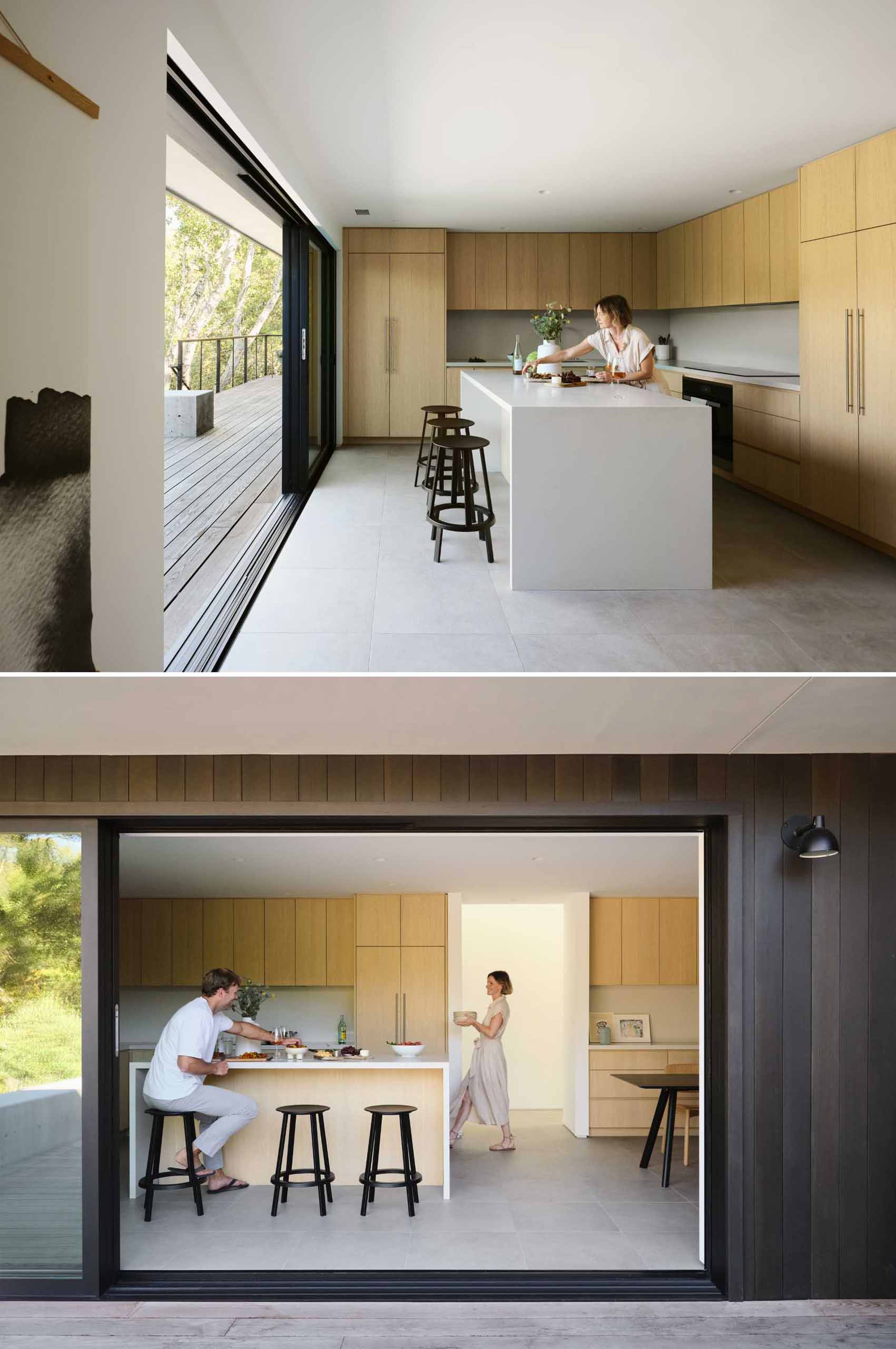 A modern kitchen with wood cabinets and an island, opens up to the deck through a sliding door.