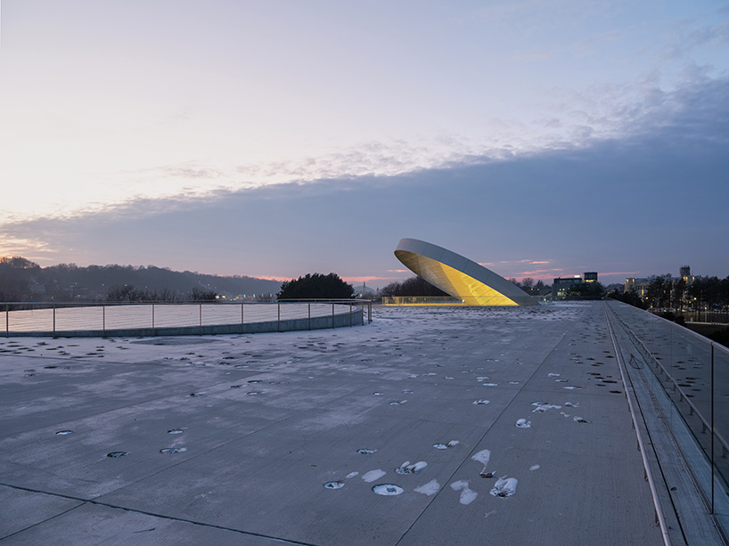 tilted reflective disk sits atop SMAR's science island museum in nemunas, lithuania