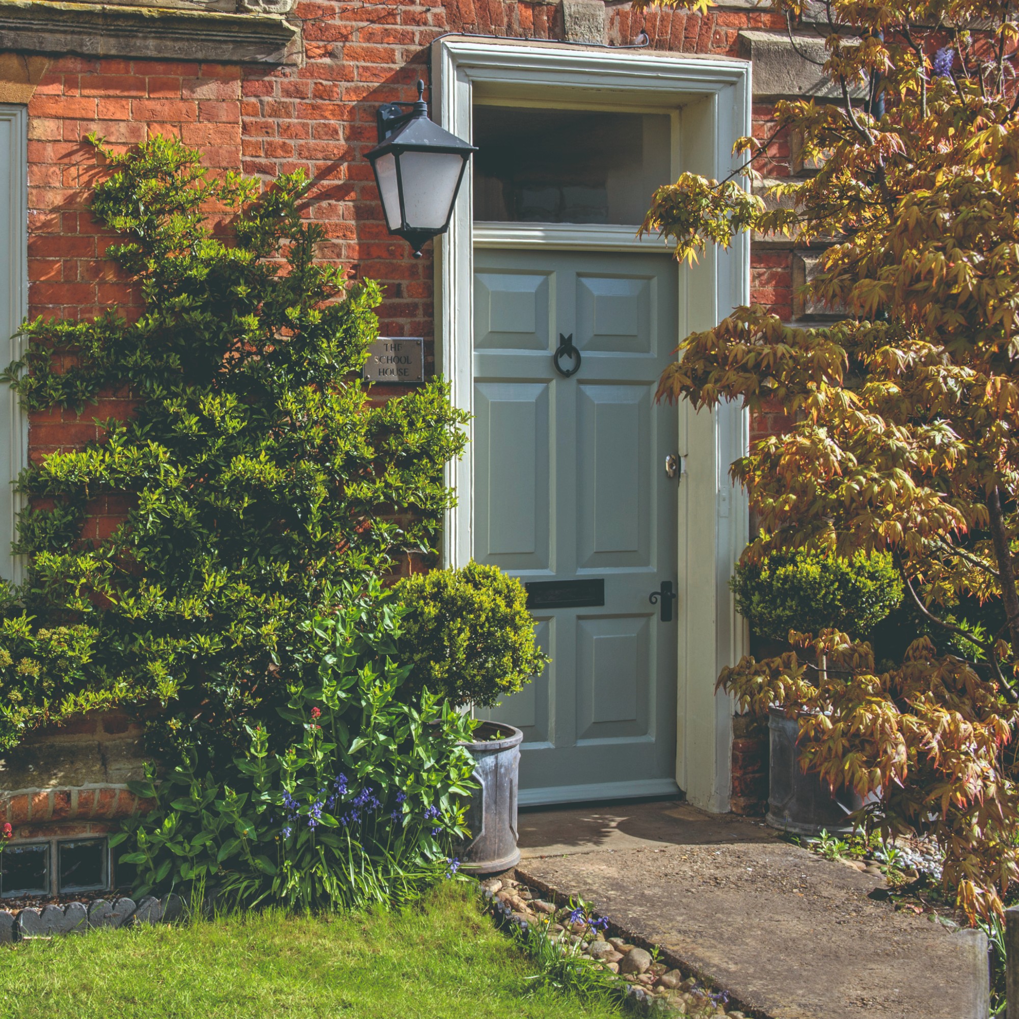A red brick house with a grey front door and a large lantern-style wall light