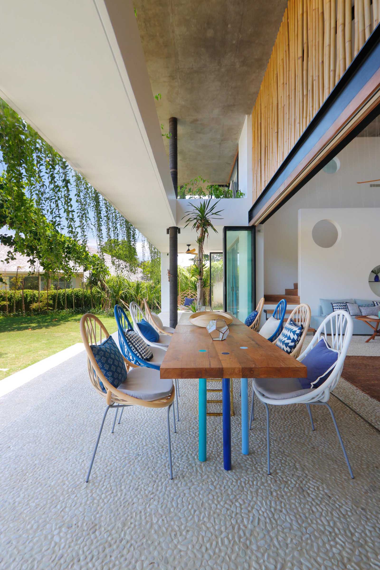 At the heart of this covered outdoor dining area is a striking wooden table that anchors the space with its bold, natural grain and substantial presence. The table’s clean and rectangular lines give it a handcrafted, feel, the kind of piece that invites long, leisurely meals. 