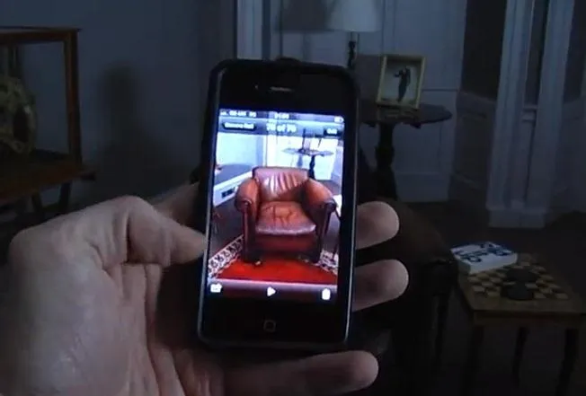 A hand holding a smartphone displaying a photo of a brown leather armchair in a dimly lit room.