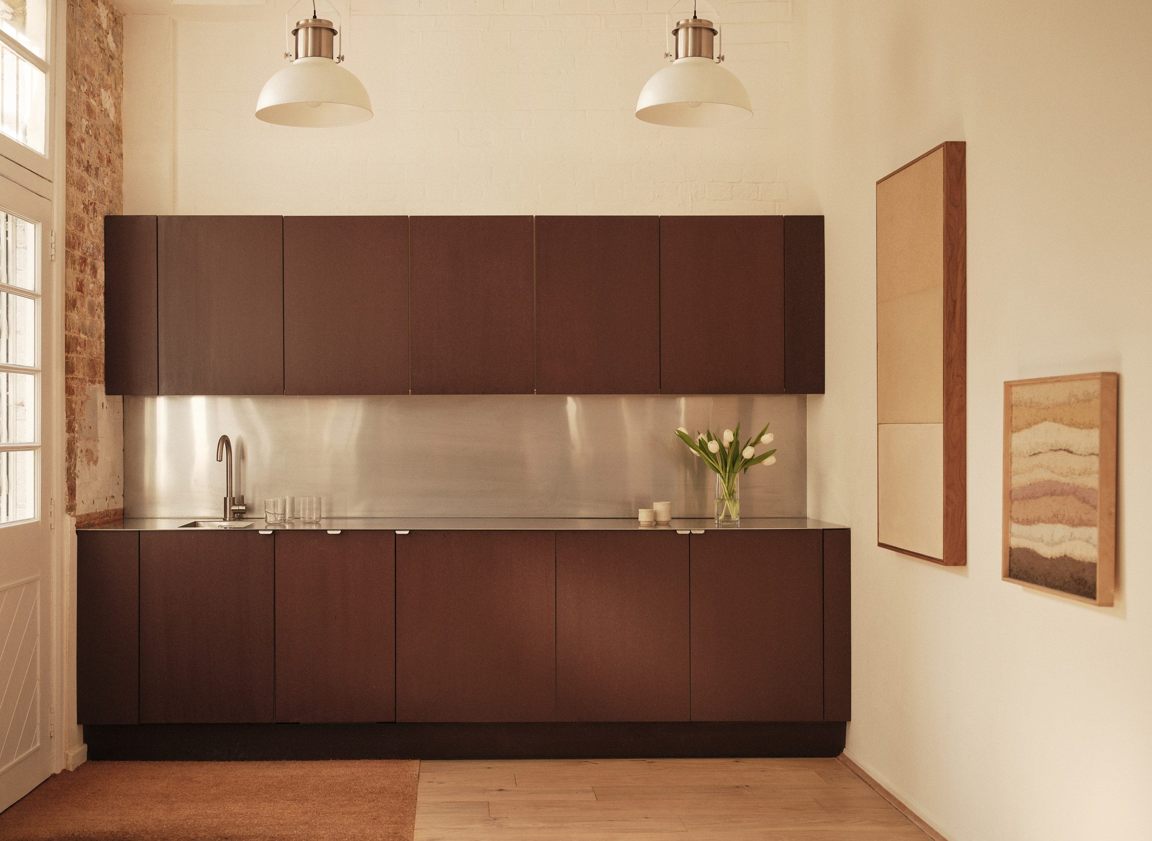 Brown-fronted kitchen in workspace with large factory windows