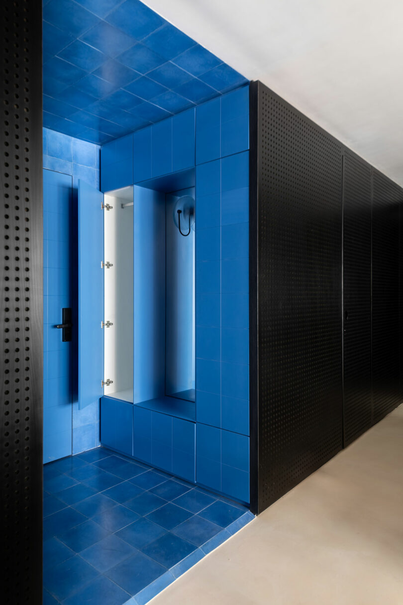 Modern bathroom with bright blue tiled walls and shower area, contrasted by black perforated panels and a light-colored floor.