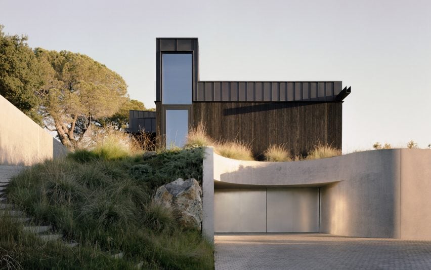 Residence with a concrete lower floor that curves to form a driveway and a dark-coloured upper level