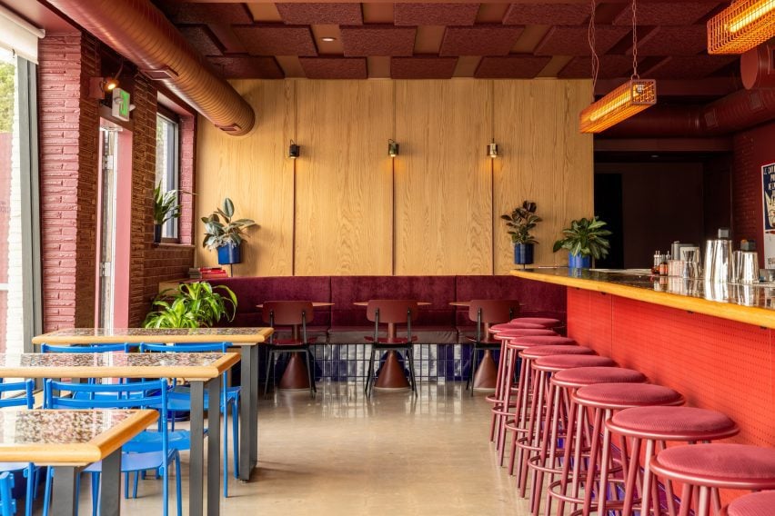 Bar interior with blue chairs against dining tables and red stool along the bar