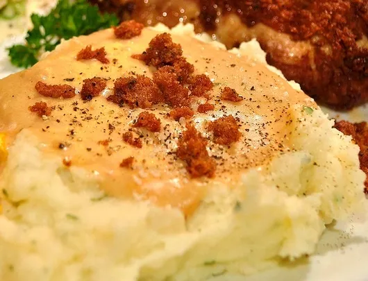 Mashed potatoes topped with gravy and crispy bits, served with a side of vegetables.