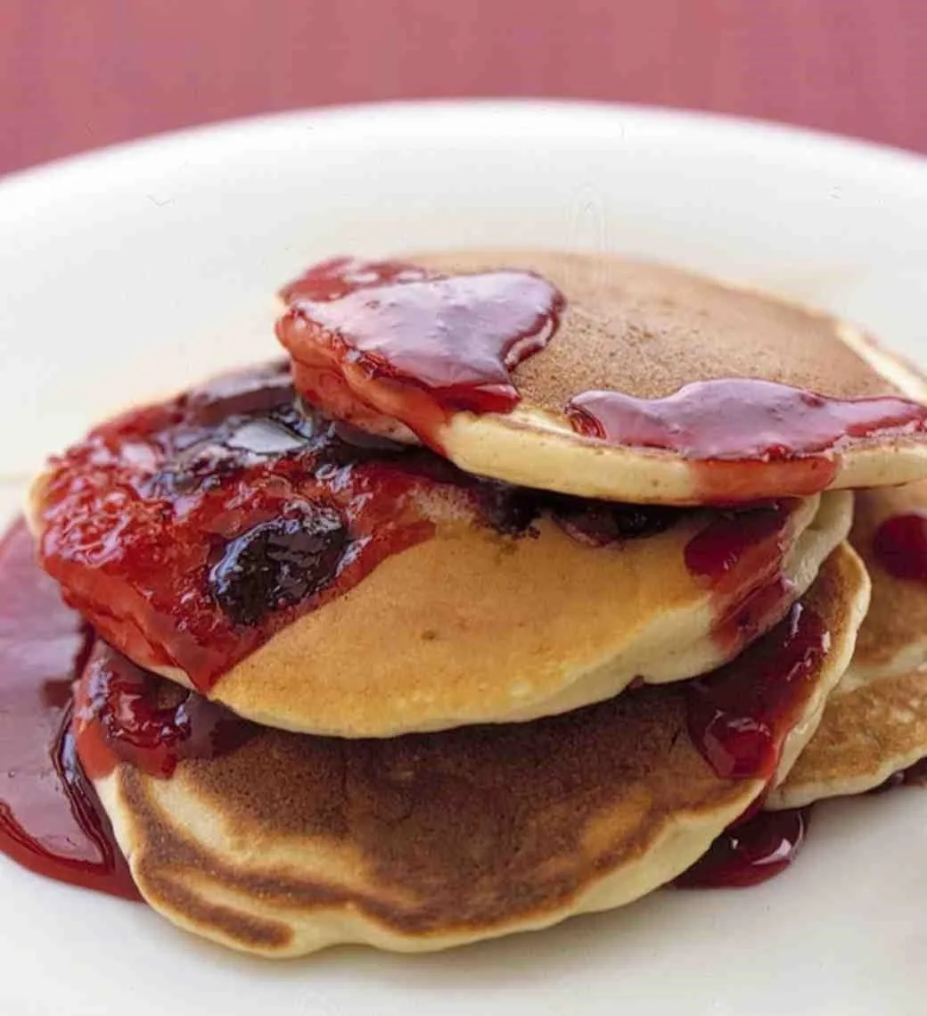 Stack of pancakes topped with syrup and strawberries.