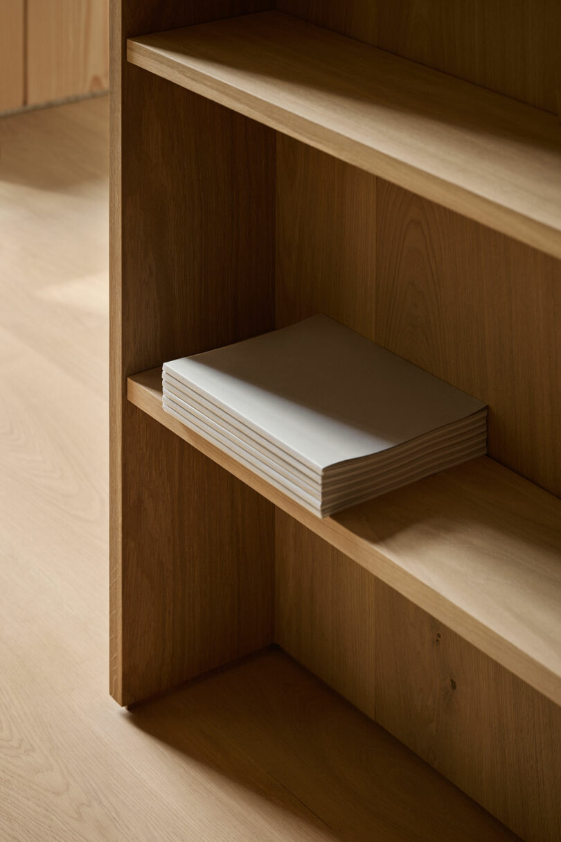 Stack of white paper placed on the middle shelf of a wooden bookcase in a room with light-colored wood flooring.