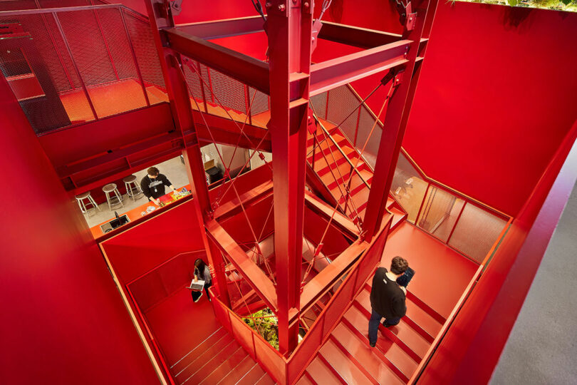 A brightly lit, industrial-style interior with red walls and staircases, featuring two people walking on the stairs and one person seated at a counter, showcases a dynamic scene perfect for a Friday Five spotlight.