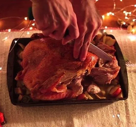 A person carving a roasted turkey on a festive table setting.