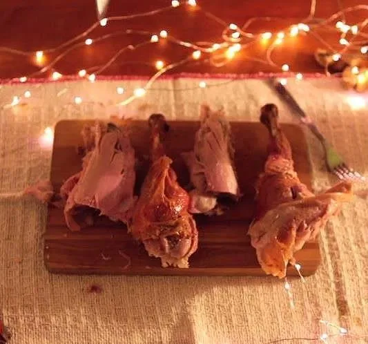 Cooked meat on a wooden cutting board with decorative lights in the background.
