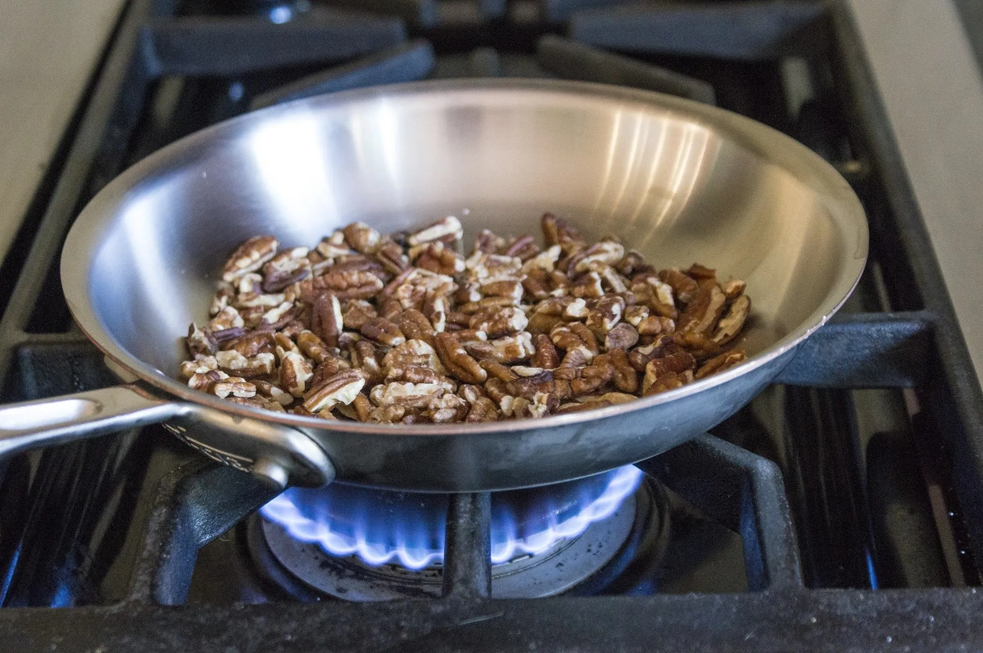 Toasted pecans in a stainless steel pan on a gas stove.