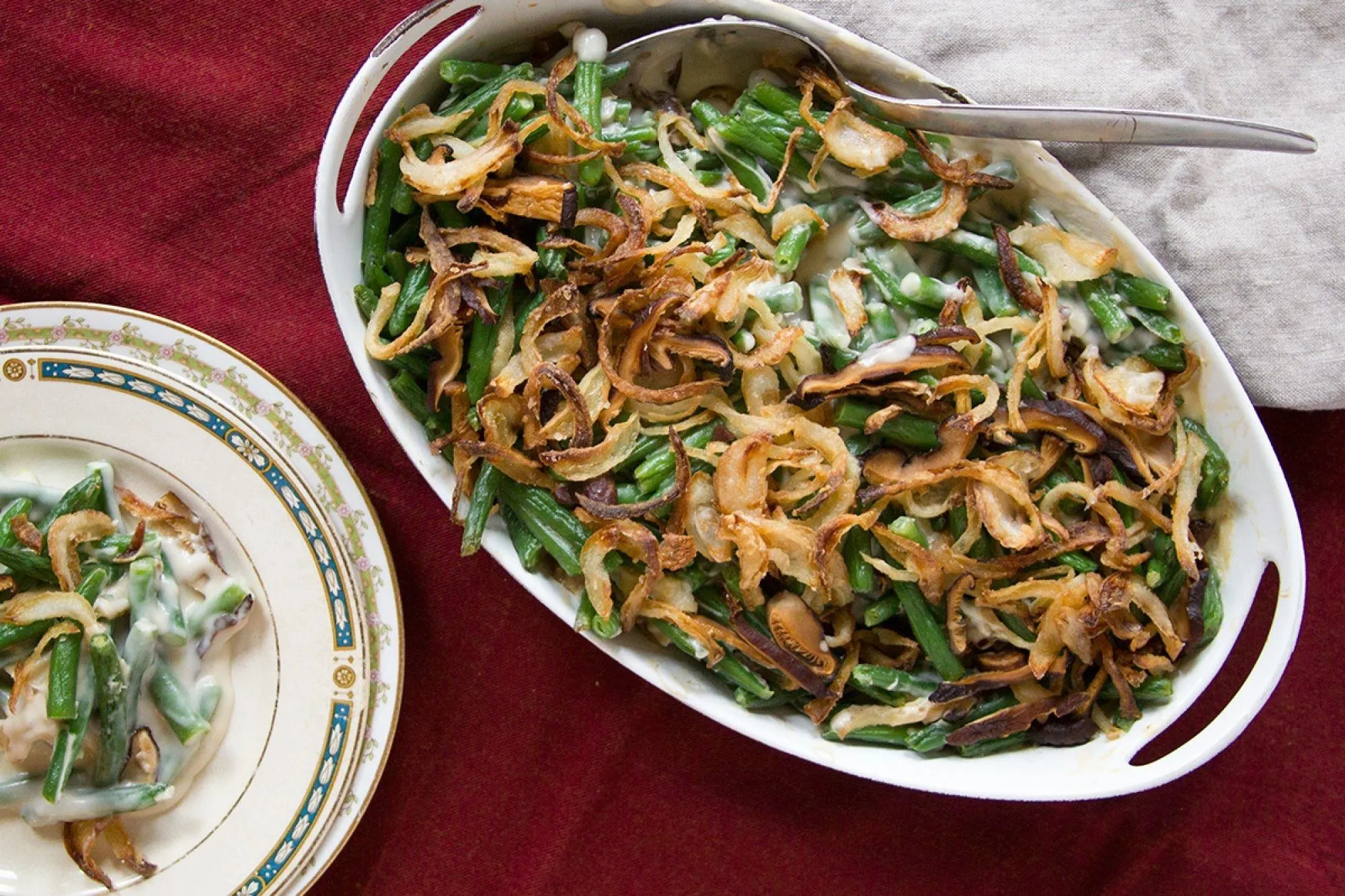 Green bean casserole with crispy onions on top, served in a white dish alongside a plate.