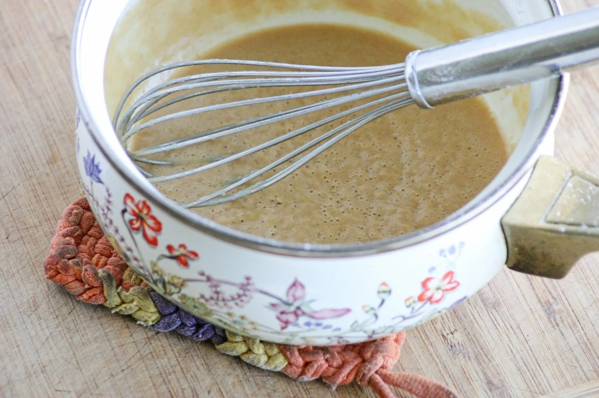 Whisk in a bowl with a mixture on a wooden countertop.