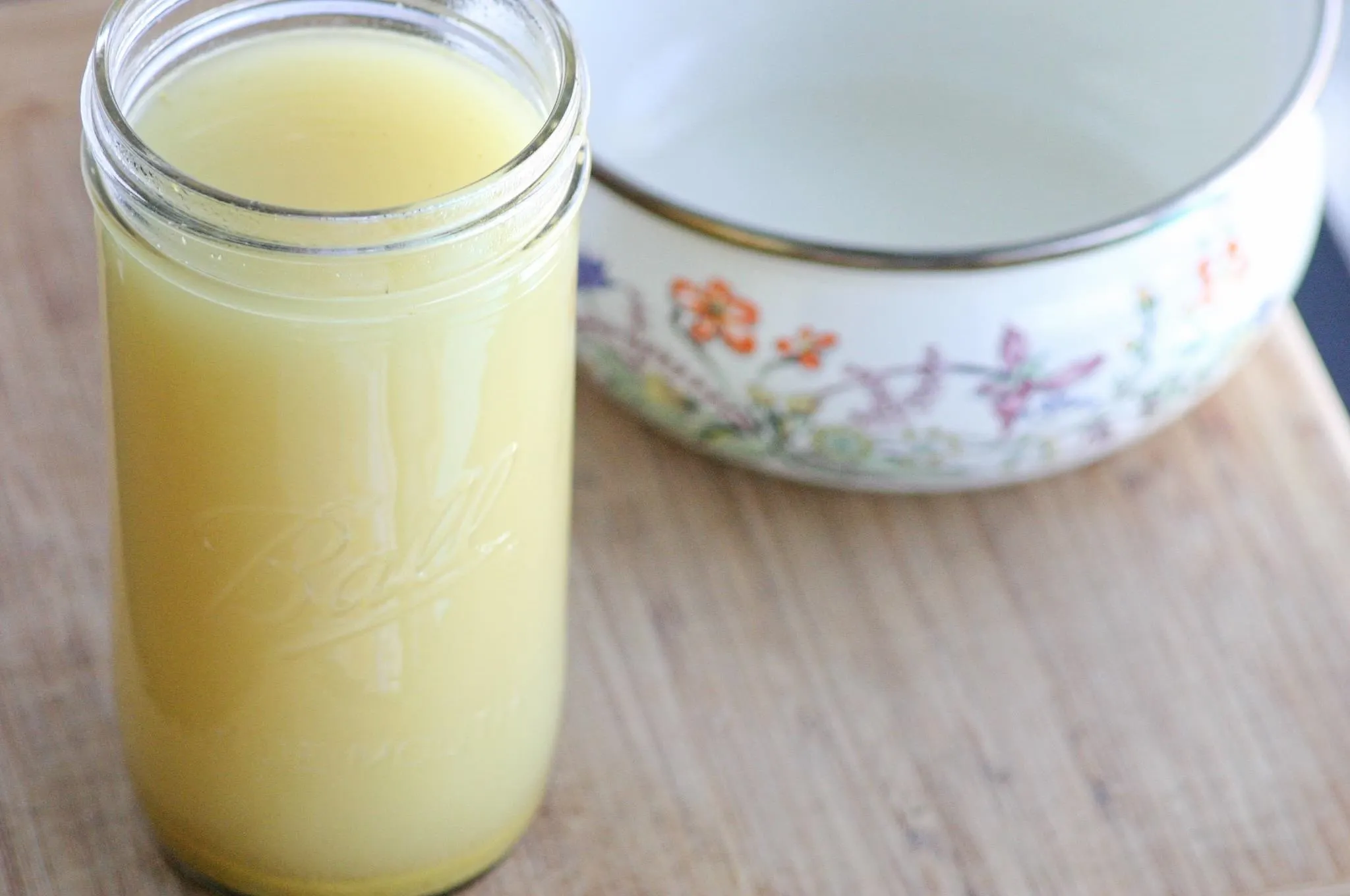Jar of liquid yellow substance on a wooden surface with an empty bowl in the background.