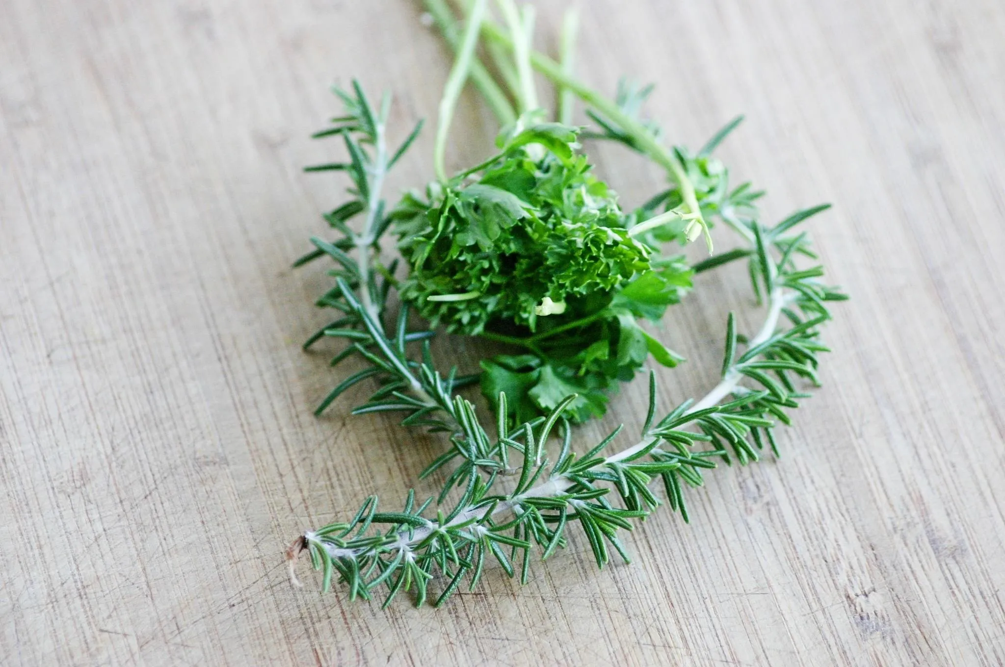 Fresh herbs: rosemary and parsley on a wooden surface.