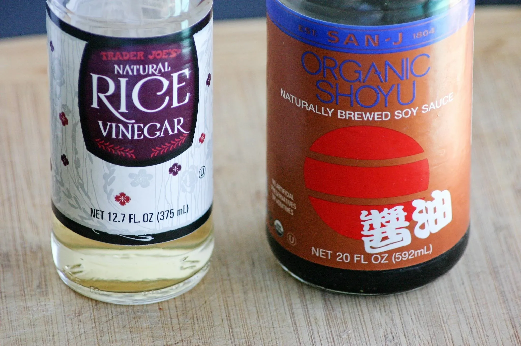 Bottle of rice vinegar and bottle of organic soy sauce on a wooden surface.
