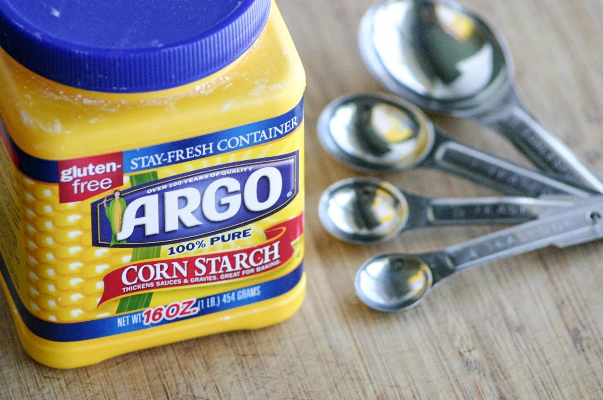 Argo corn starch container with measuring spoons on a wooden surface.