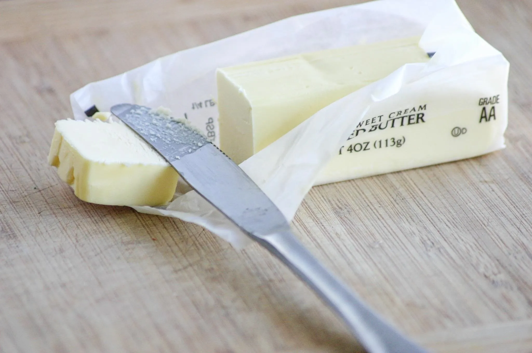 Butter stick partially wrapped with a knife on a wooden cutting board.