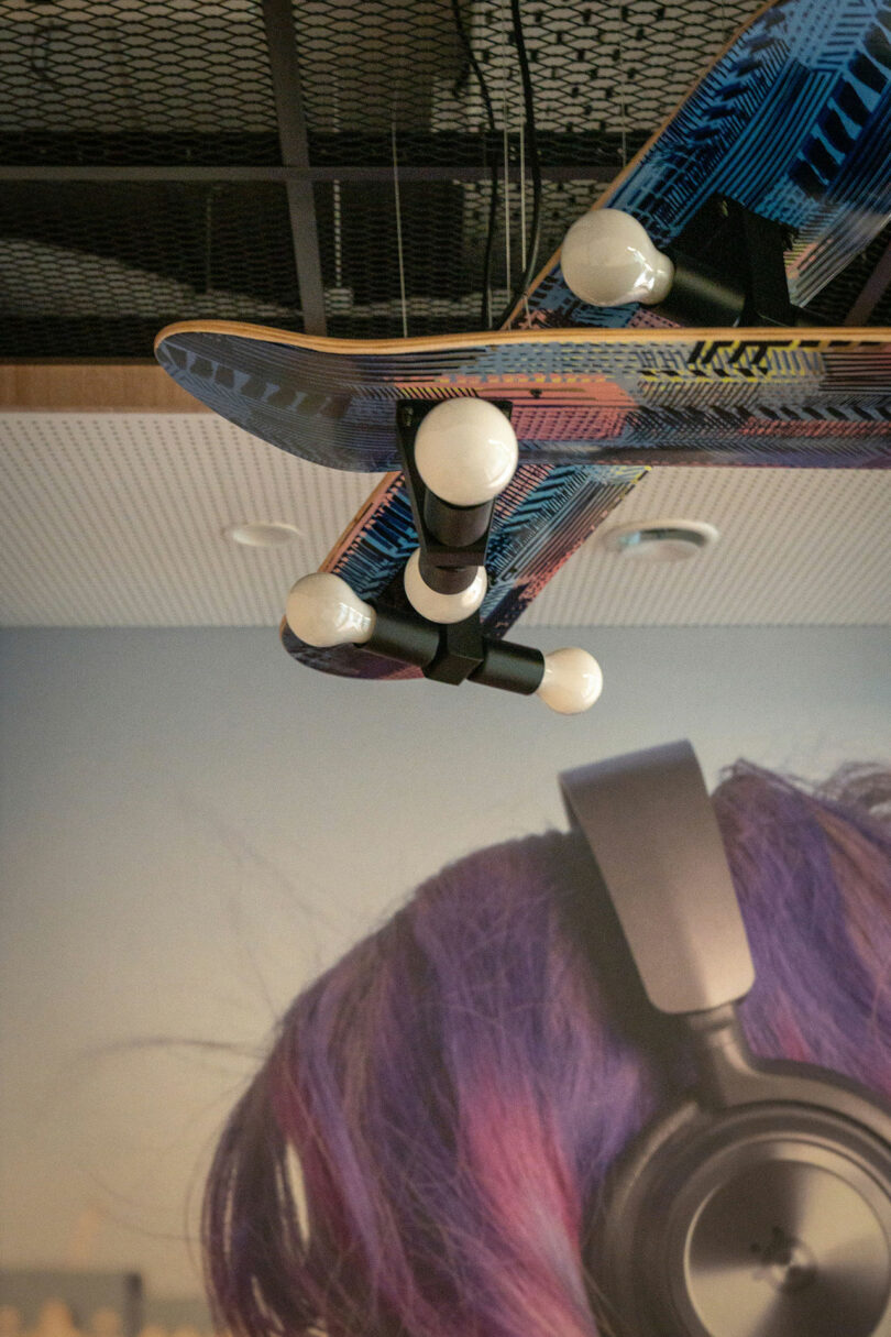 A BIT CREATIVE touch: a skateboard mounted upside down on the ceiling with light bulbs attached to its wheels, displayed above a wall mural of a person wearing headphones.